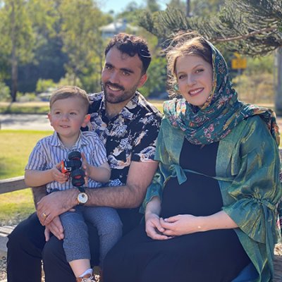 Man, woman and child sitting on park bench smiling at camera.